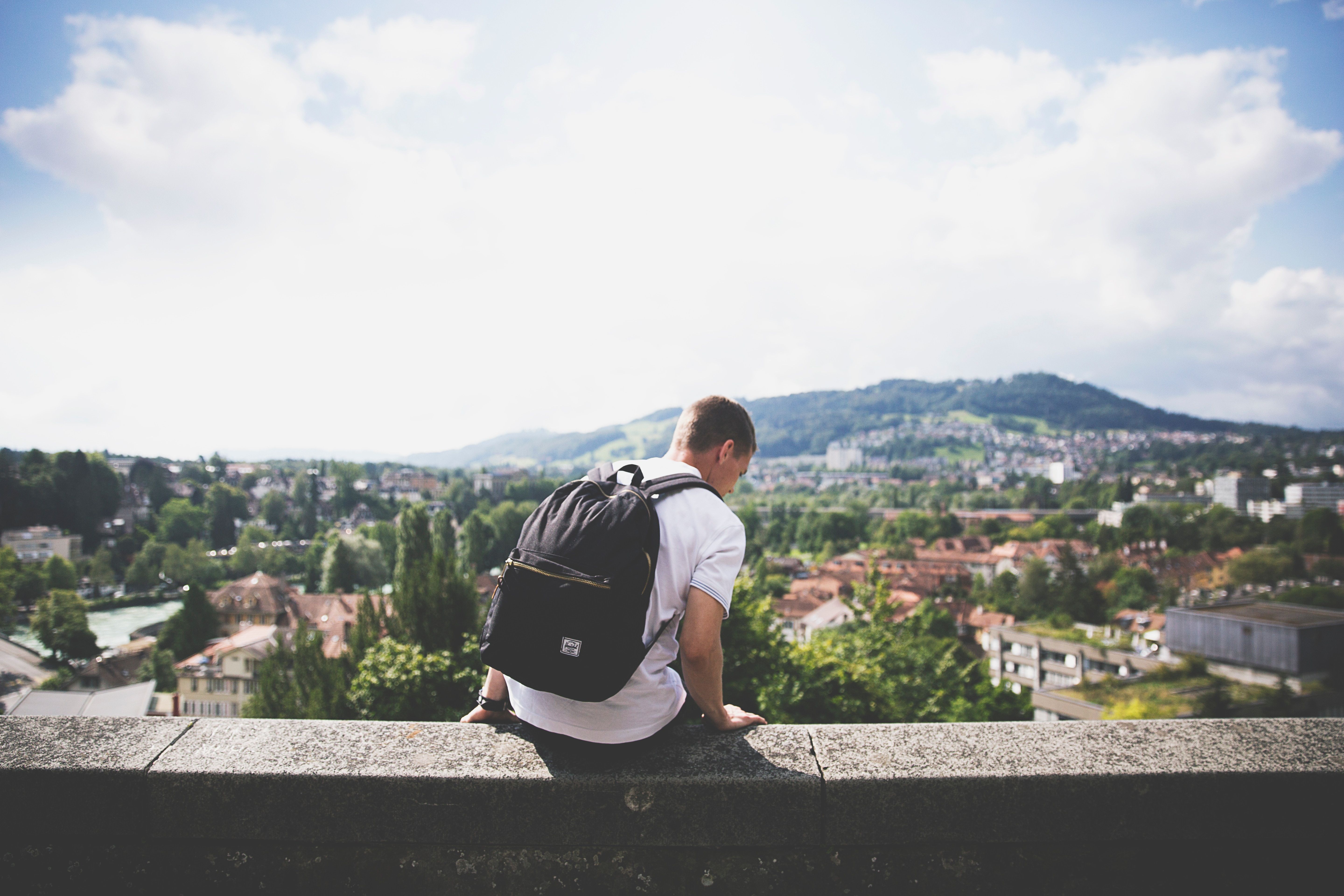 Boy sat on concrete wall with black backpack