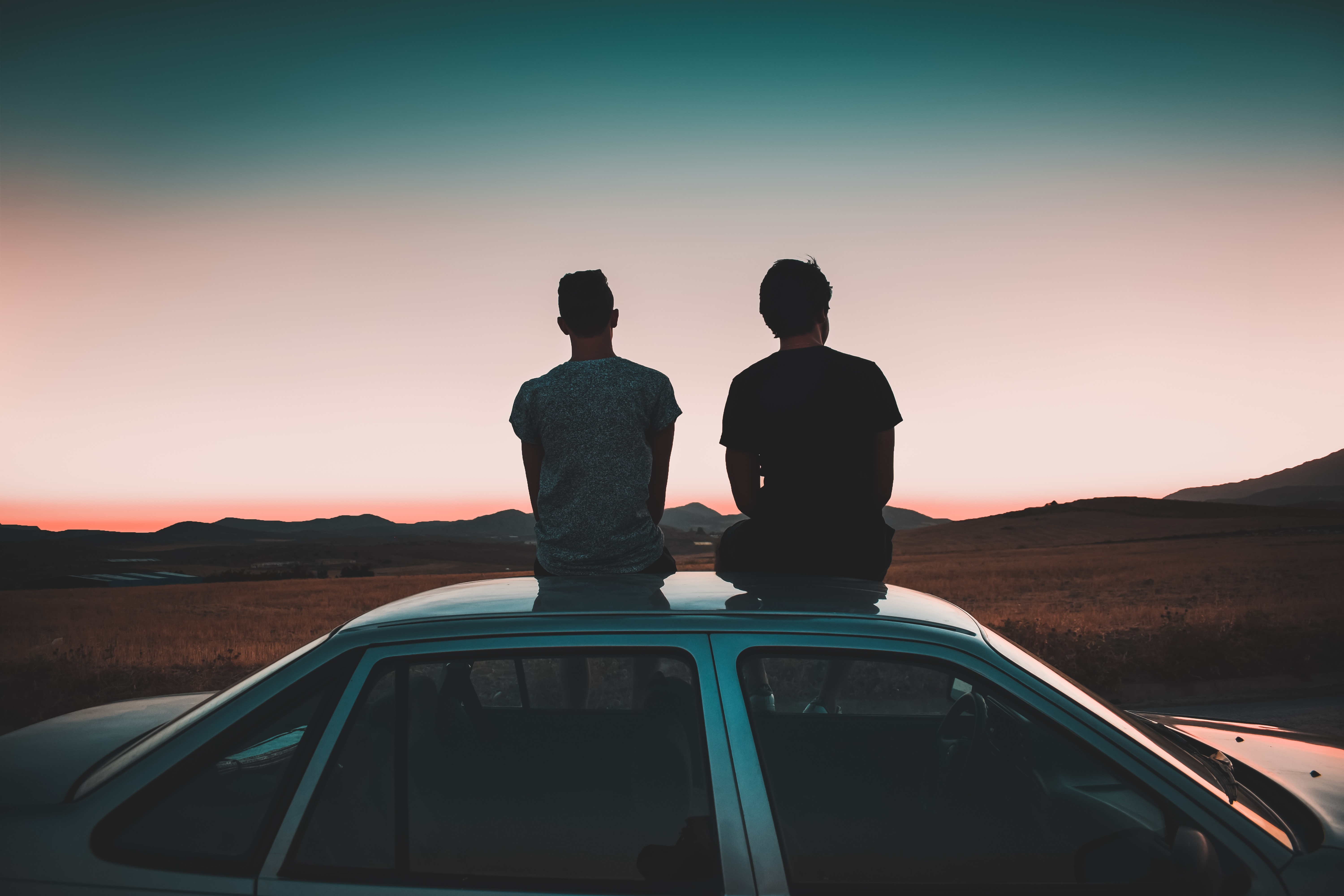 Two men sat on a car roof.